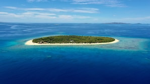 An aerial view of a tropical island with clear turquoise waters, a sandy beach, and lush greenery. - Serenity Sands Island Glamping (Kadavulailai Island)