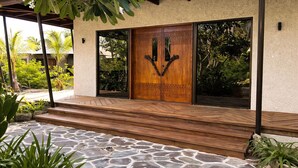 Un edificio moderno con una puerta de madera grande, escalones de piedra y una zona de entrada cubierta.