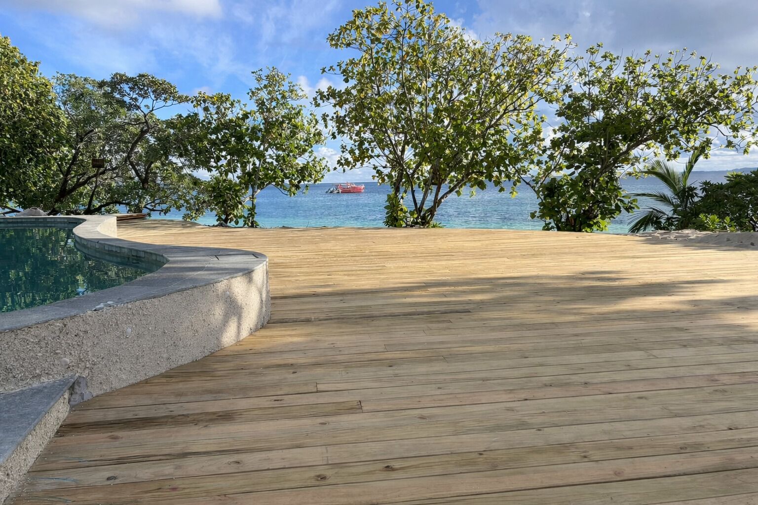 Una terraza de madera con piscina, rodeada de árboles y vistas a un cuerpo de agua.