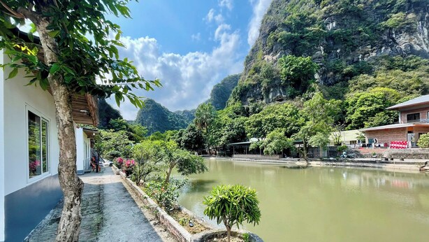 Un hotel a orillas del río con un paseo pavimentado, un pequeño jardín y vistas de las montañas circundantes.