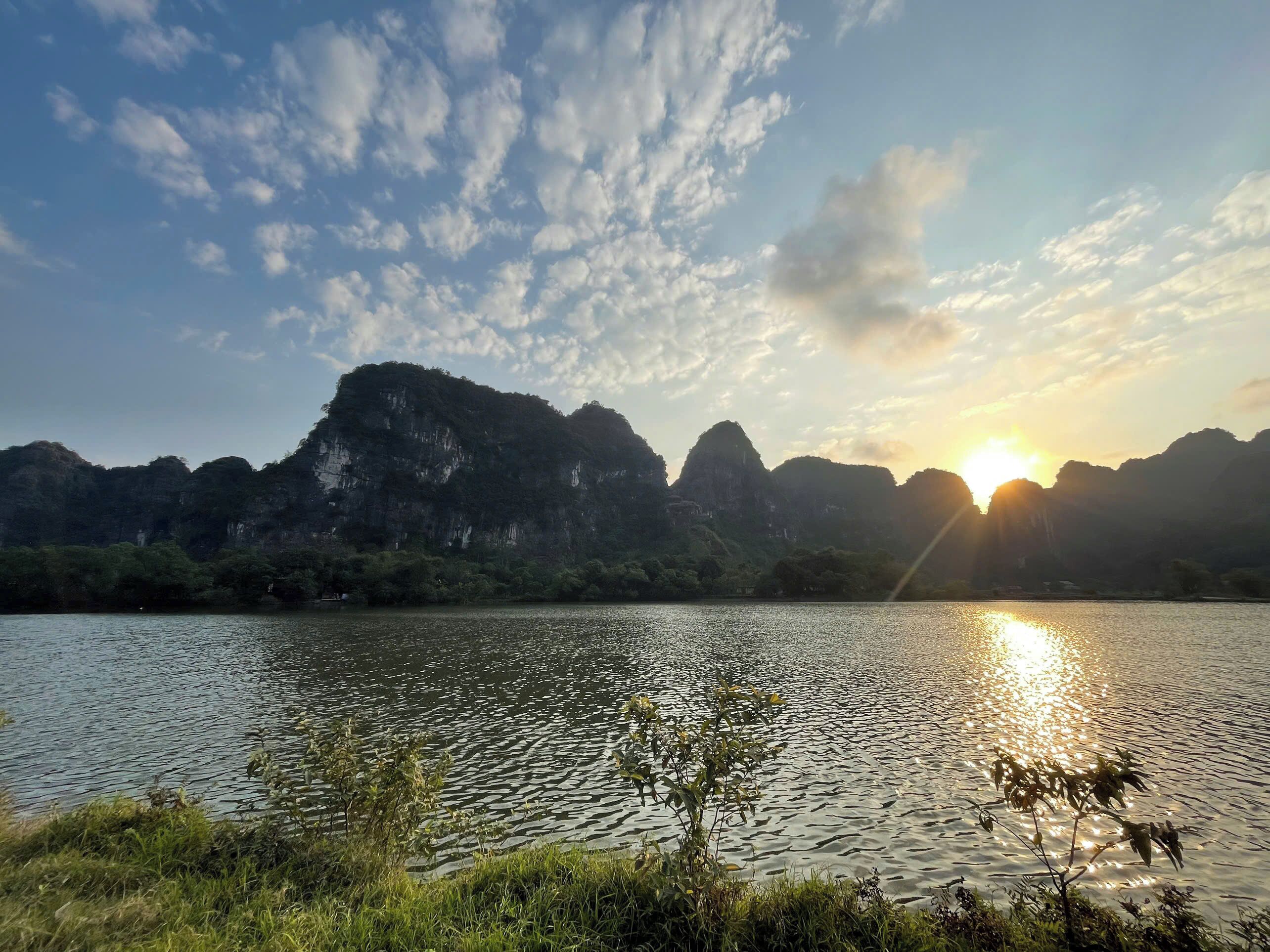 Un lago tranquilo con montañas al fondo y el sol poniéndose o saliendo.