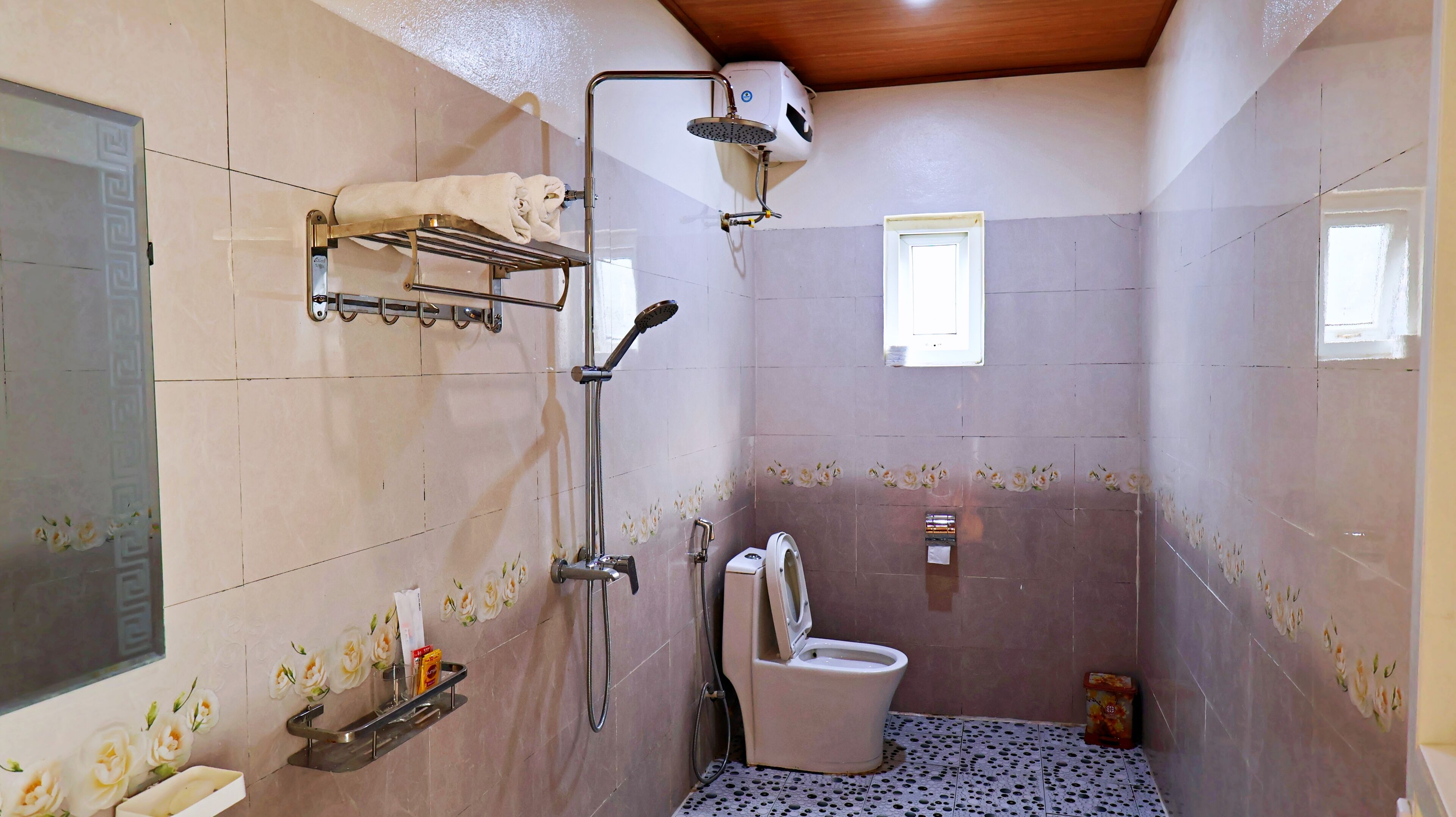 A bathroom with a shower, toilet, towel rack, and a small window.