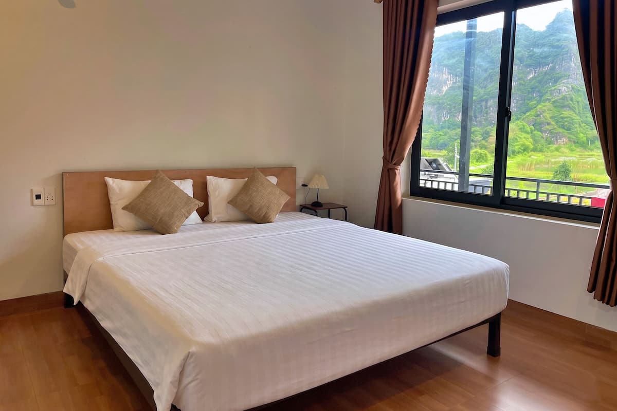 Una cama bien hecha con cabecera de madera, una lámpara de noche y una ventana con cortinas.