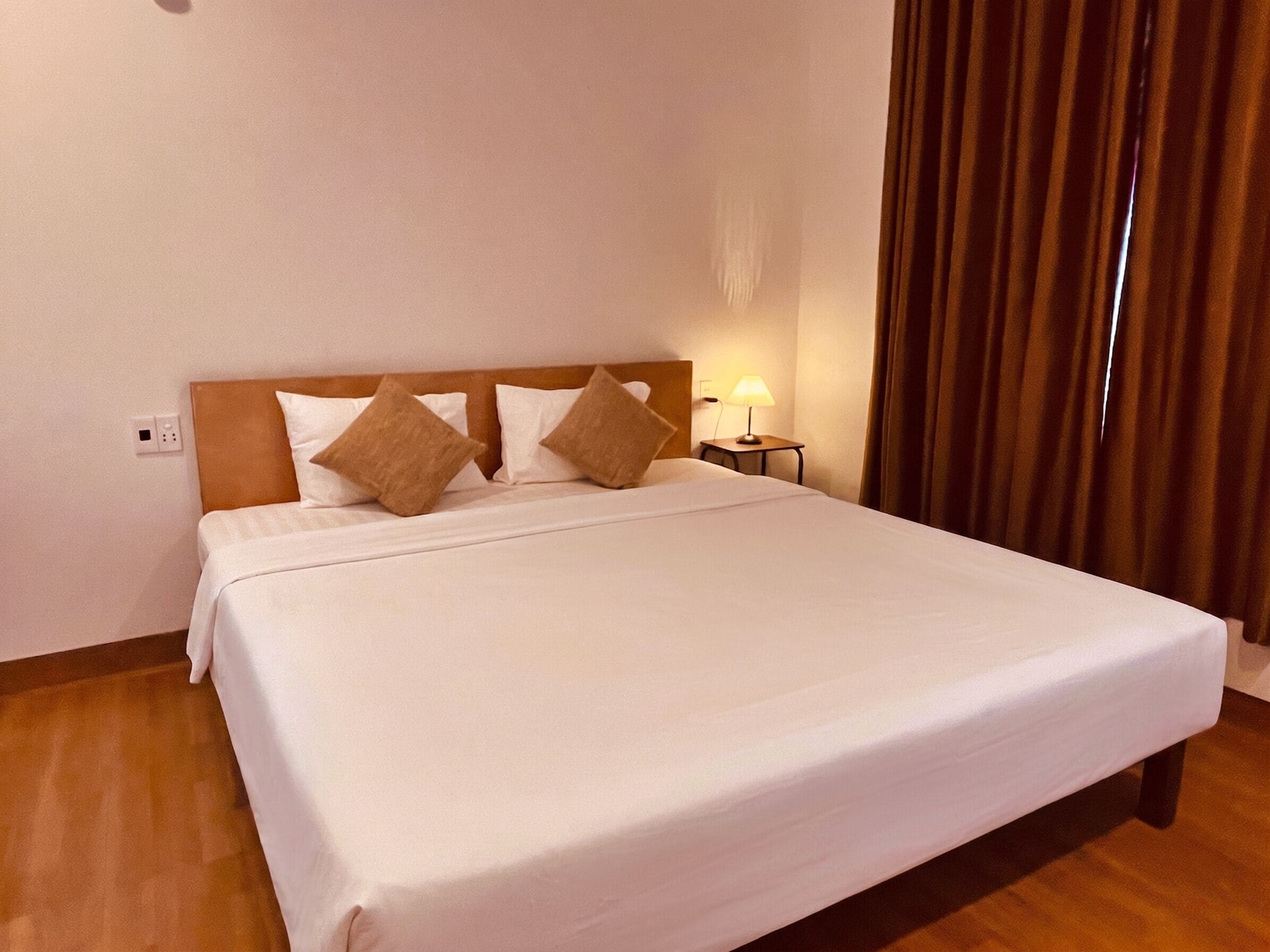 Una cama bien hecha con cabecera de madera, una lámpara de noche y un enchufe en la pared.