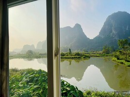 Visão pela janela de uma paisagem natural com um corpo d'água calmo, vegetação e montanhas ao longe.