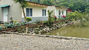 Un edificio rústico con techo de paja, un pequeño jardín y un río al frente.