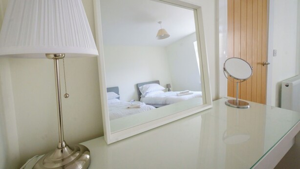 A hotel room with a bed, a bedside lamp, a mirror, and a wooden door. - Gorgeous, fully refurbished centrally located cosy cottage (Hawick)