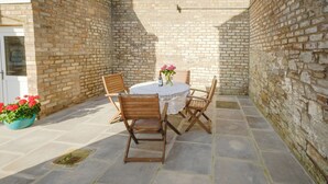 A patio with a round table and four wooden chairs, surrounded by stone flooring and brick walls. - Gorgeous, fully refurbished centrally located cosy cottage (Hawick)