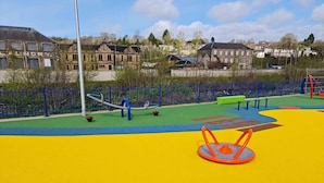 A playground with colorful play equipment and a blue fence. - Gorgeous, fully refurbished centrally located cosy cottage (Hawick)