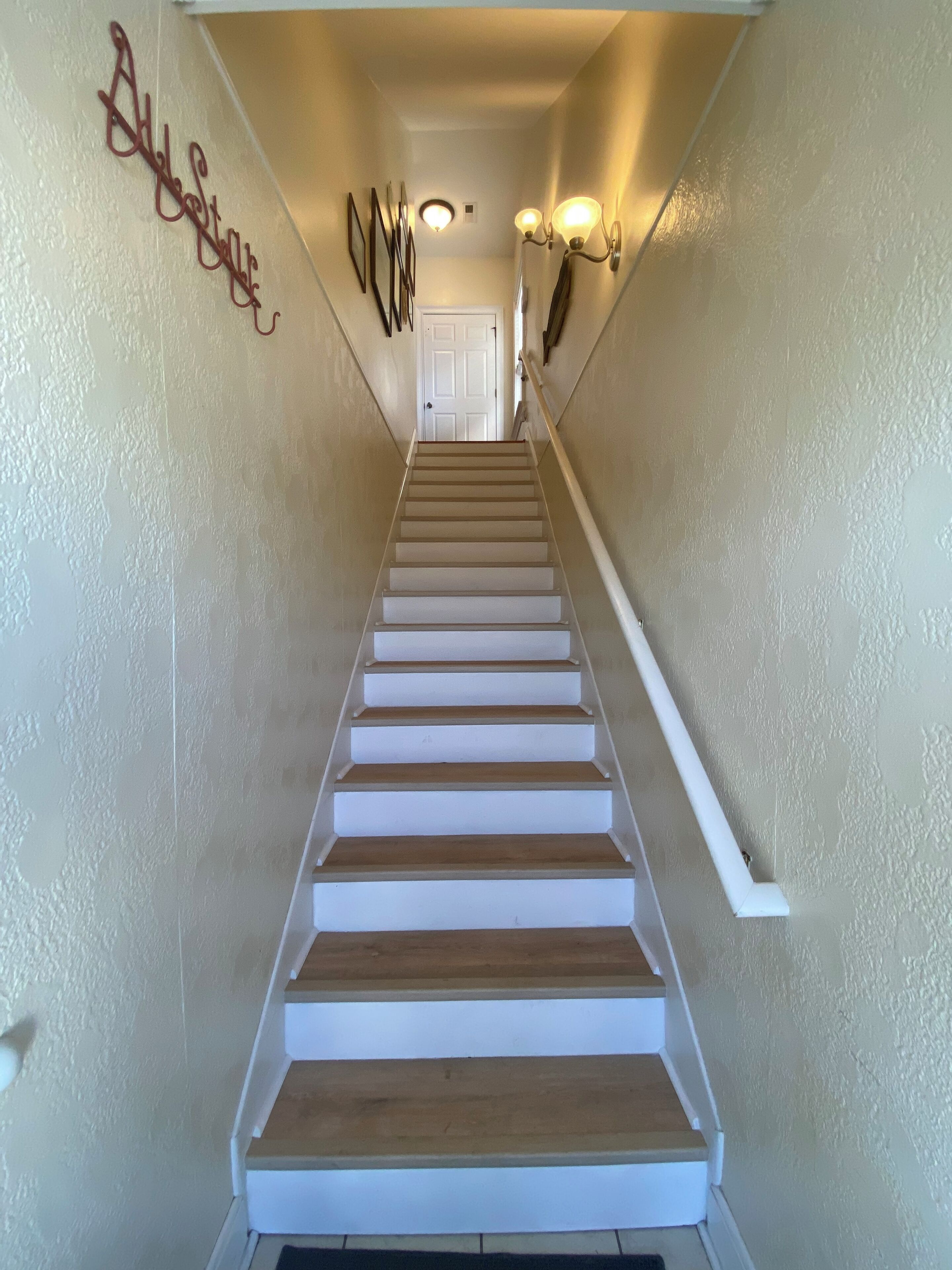 Un escalier avec des marches en bois et des rampes blanches, menant à une porte située en haut.