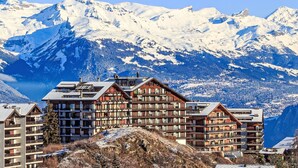 A mountain lodge with multiple floors and balconies, surrounded by snow-covered peaks and a clear sky. - Nice apartment for 4 guests with WIFI, TV and balcony (Basse-nendaz)
