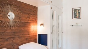 A bedroom with a wooden headboard, a round mirror, a bed with white bedding, a blue accent wall, a wardrobe, and a framed picture on the wall. - Nice apartment for 4 guests with WIFI, TV and balcony (Basse-nendaz)