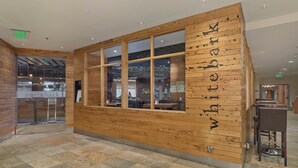 Un mostrador de recepción de madera con una separadora de vidrio, un cartel que dice "white bark" y un piso de baldosas.