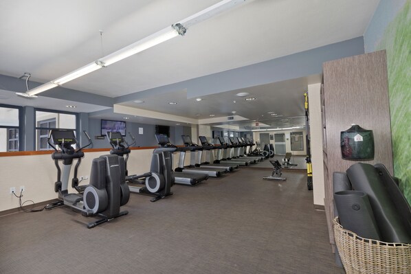 A gym with multiple treadmills and exercise equipment, a reception area with a TV, and a large window providing natural light.