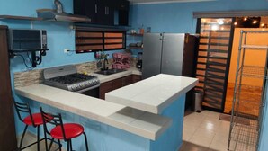A compact kitchen with a gas stove, a microwave, and a refrigerator. There are two red bar stools and a small sink. - Comfortable & Beautiful house in Caucel (Merida)