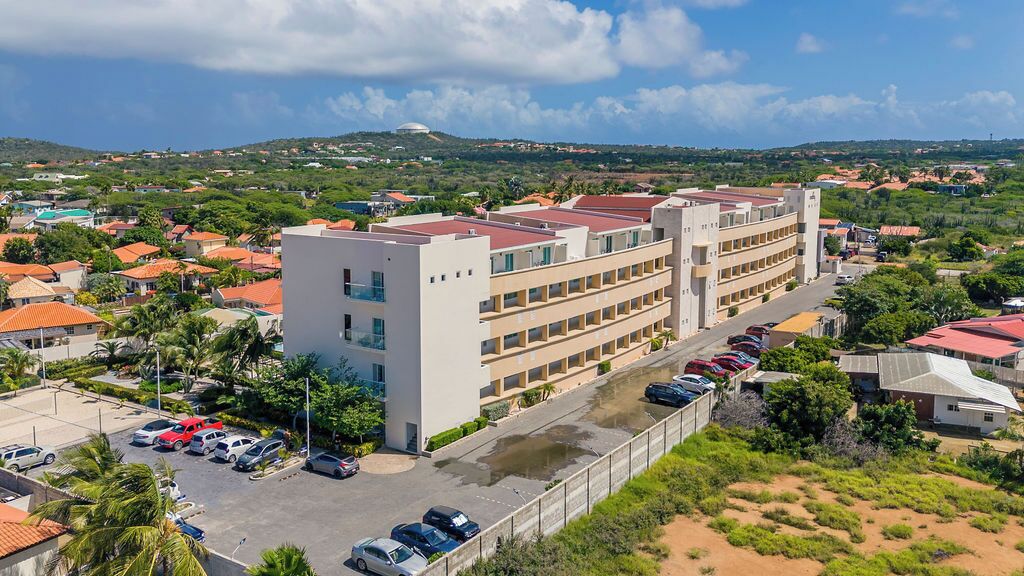 A multi-story hotel with a parking lot and a view of surrounding residential buildings and greenery.