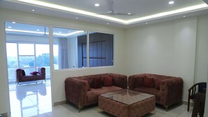 A spacious living room with a large sectional sofa, a glass coffee table, and a view of a balcony. - Hotel Veera (Mukerian)