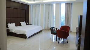 A modern hotel room with a large bed, a desk, two chairs, and a TV. - Hotel Veera (Mukerian)