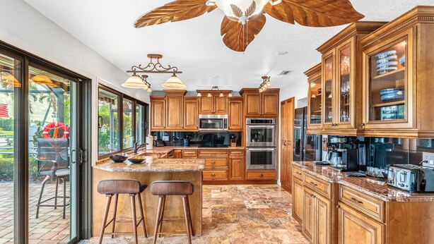 A spacious kitchen with wooden cabinets, a large island, and a view through the glass doors. - Canal Access: Boat Lift, Heated Pool & Dock (Cocoa Beach)