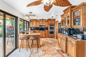 A spacious kitchen with wooden cabinets, a large island, and a view through the glass doors. - Canal Access: Boat Lift, Heated Pool & Dock (Cocoa Beach)