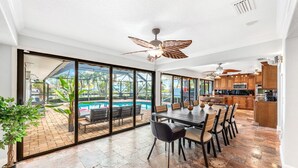 A spacious kitchen with modern appliances, a dining area with a large table and chairs, and a view of a swimming pool through large glass doors. - Canal Access: Boat Lift, Heated Pool & Dock (Cocoa Beach)