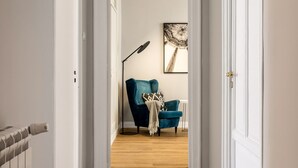 A hallway with a blue armchair, a floor lamp, and a framed artwork on the wall. - Constance Luxury Apartment by DomuSicily (Palermo)