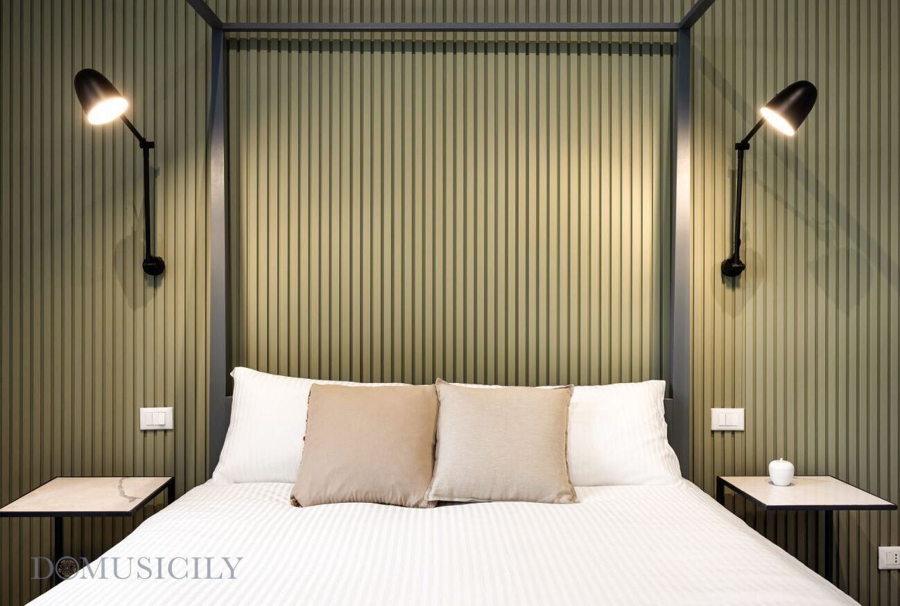 A neatly made bed with two pillows, flanked by two bedside tables with lamps, in a room with vertical paneling on the walls.