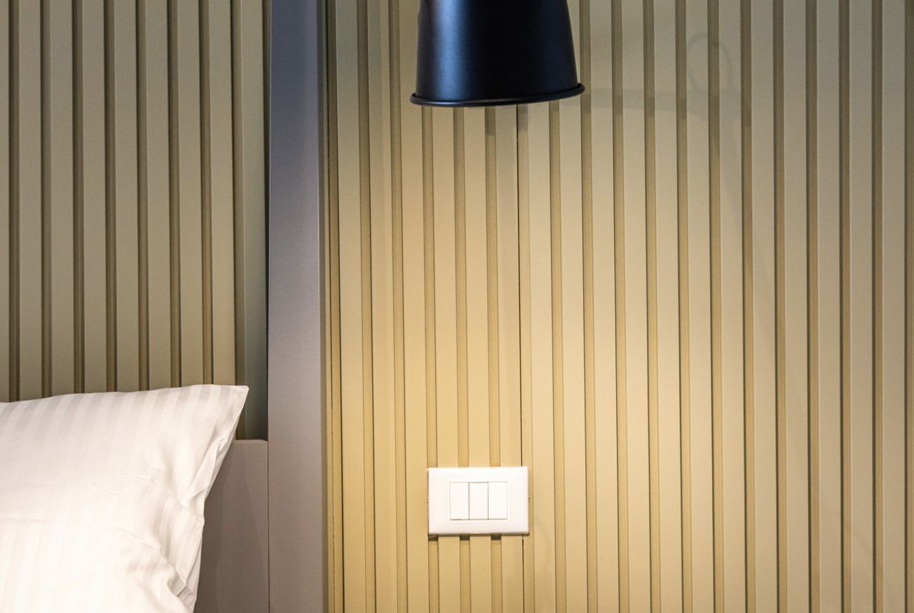 Een kamer met een bed, een lichtschakelaar aan de muur en verticale panelen.