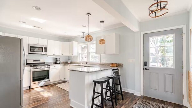 Une cuisine moderne avec des meubles blancs, un îlot central doté de tabourets, un four à micro-ondes, une cuisinière et un réfrigérateur.
