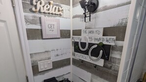 A bathroom with a rustic design, featuring a wooden wall with horizontal stripes, a towel rack, a towel shelf, and a light fixture.