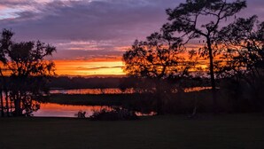 A sunset over a lake with trees and a bench in the foreground.