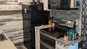 A modern kitchen with a black refrigerator, stainless steel oven, and microwave. There is a wooden countertop with a coffee machine and a cabinet above it.