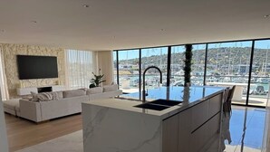 Une cuisine moderne dotée d’un grand îlot central, d’un téléviseur encastré et offrant une vue sur un port de plaisance.