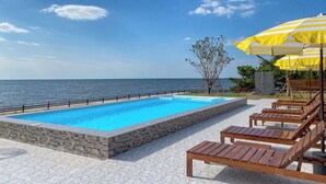 A swimming pool with a stone border, wooden lounge chairs, and a yellow umbrella. - Charome Resort (Khlong Yai)