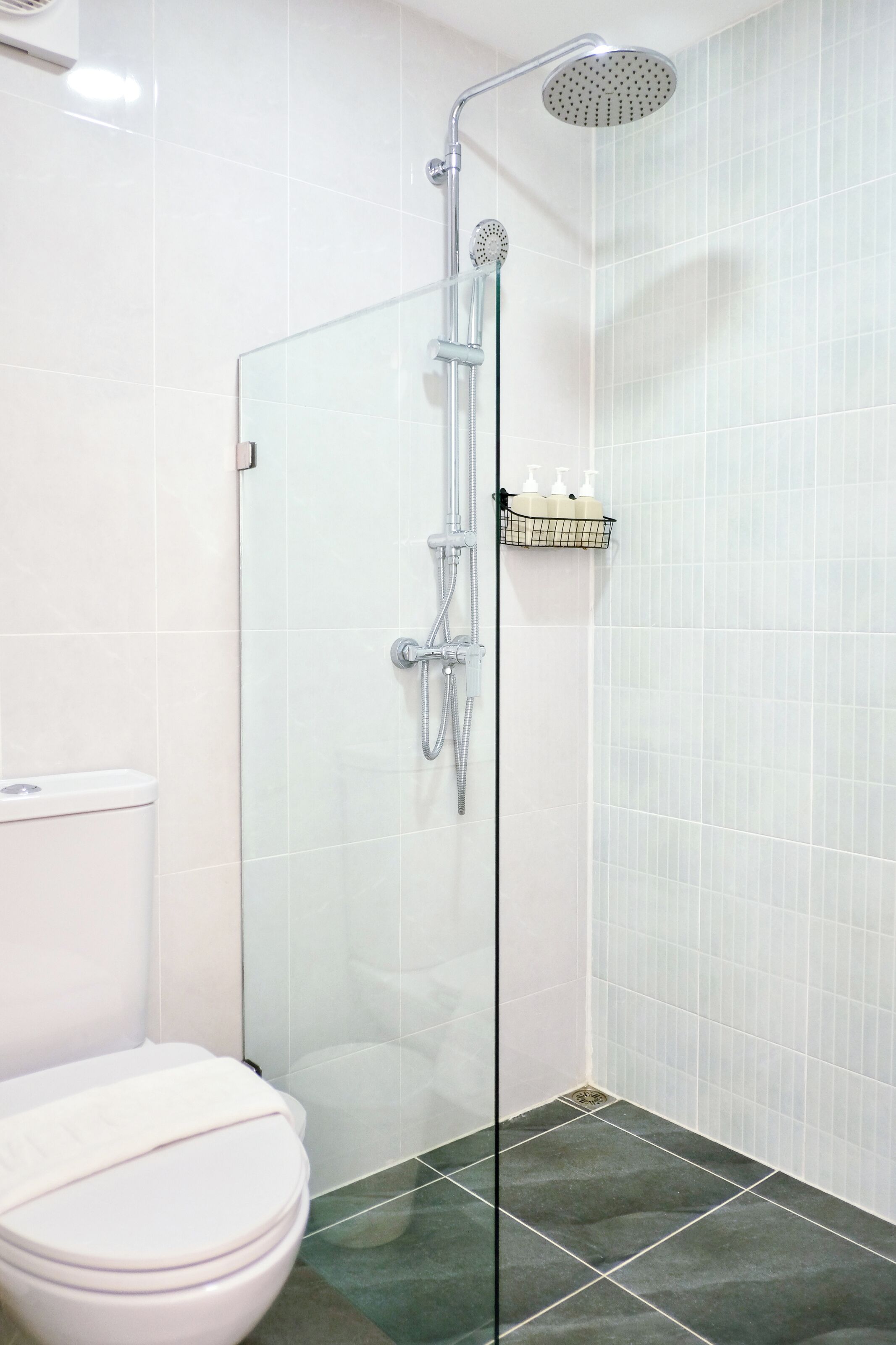 Une salle de bain moderne avec une douche à parois de verre, des toilettes et une étagère contenant des articles de toilette.