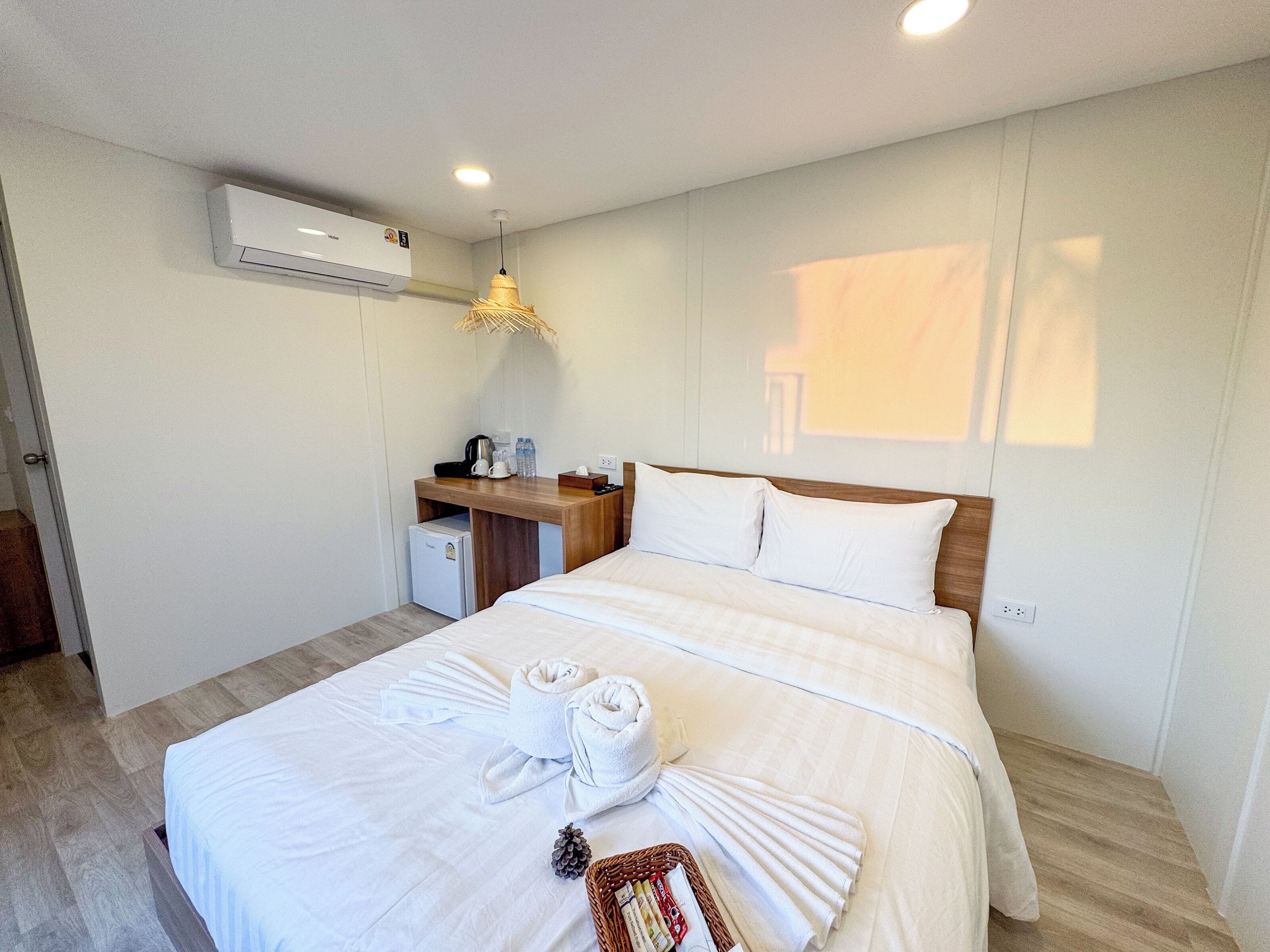 A hotel room with a bed, a desk with a coffee maker, a small fridge, and an air conditioner.