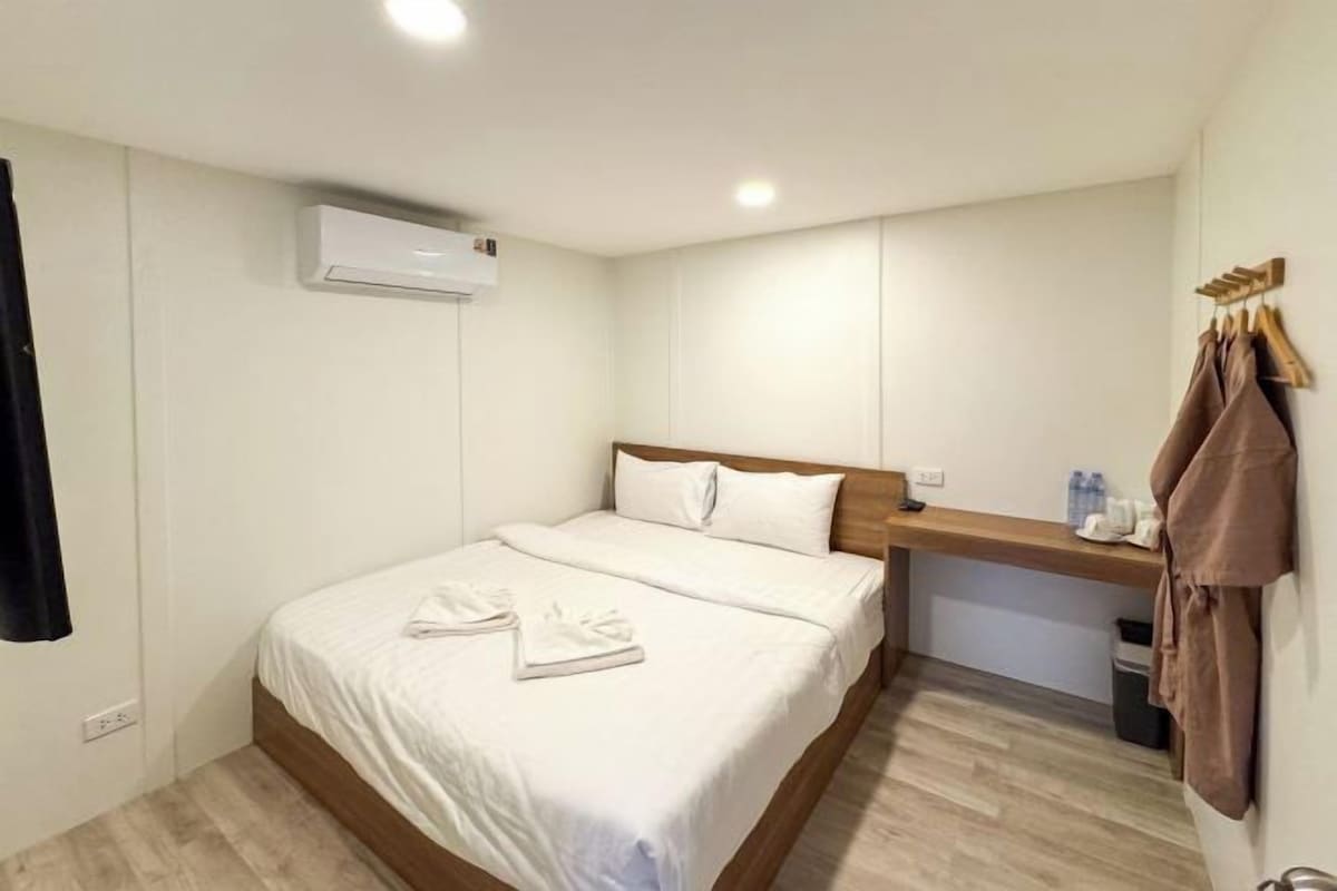 Habitación de hotel con cama, cabecera de madera, mesita de noche con lámpara y aire acondicionado instalado en la pared.