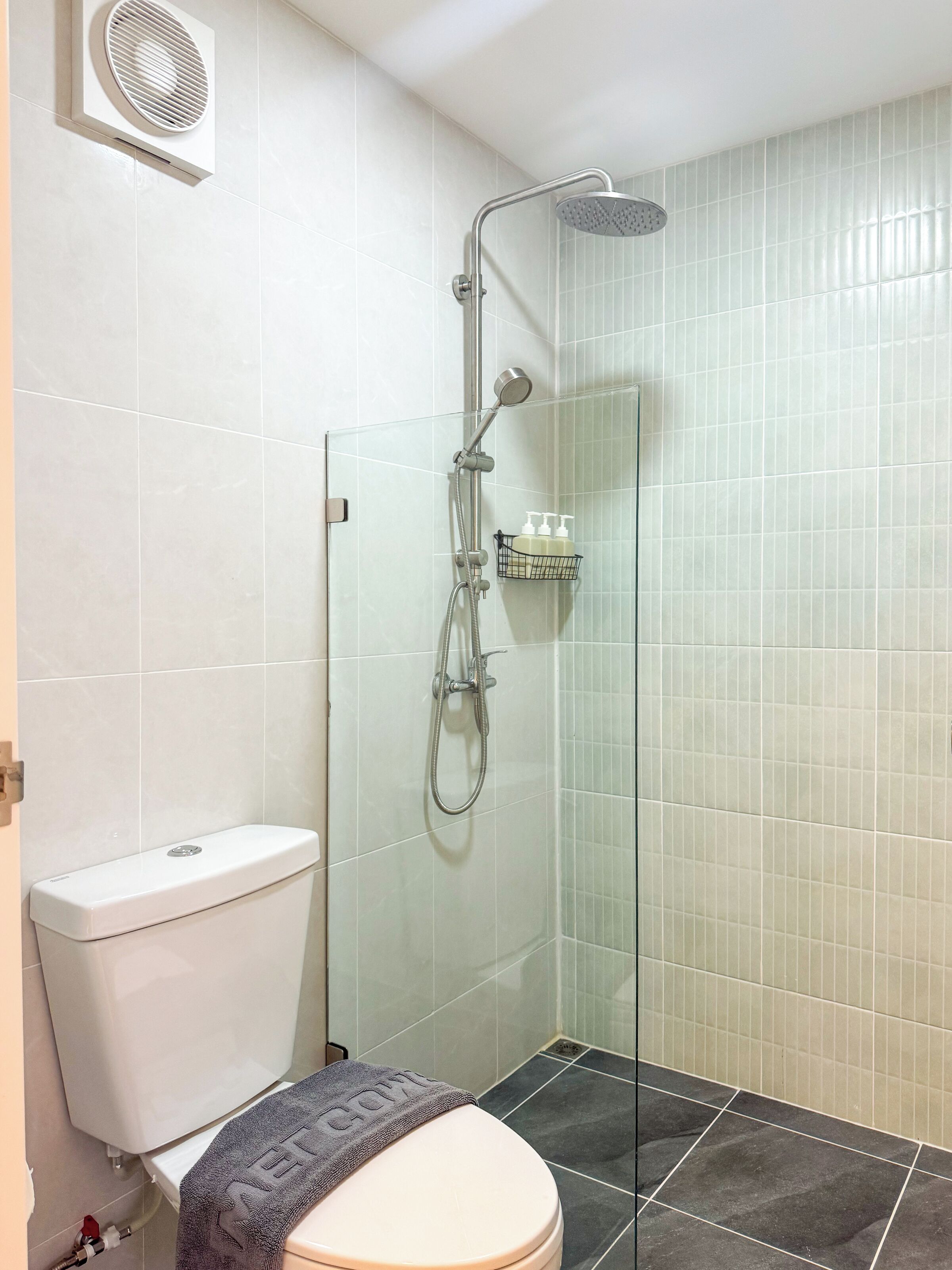 A bathroom with a glass-enclosed shower, a toilet, and a shelf with toiletries.