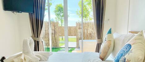 A hotel room with a bed, a TV mounted on the wall, and a view of the outside through a glass door.