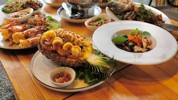 A table set with various dishes and a hot pot, overlooking a beach with a wooden fence. - Charome Resort (Khlong Yai)