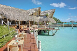 Overwater bungalows elevated on stilts offer a view of the surrounding sea from wooden deck areas with wicker furniture.