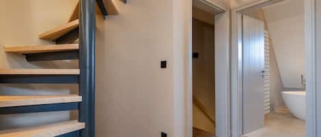 Un intérieur moderne avec un escalier en colimaçon, une salle de bain dotée d’une baignoire et un couloir menant à une autre pièce.