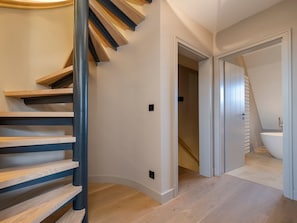 Un interior moderno con una escalera espiral, un baño con bañera y un pasillo que lleva a otra habitación.