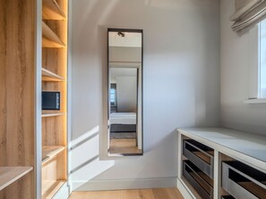 Un pasillo estrecho con estanterías de madera en un lado y una consola blanca en el otro. Un espejo grande abarca todo el ancho del pasillo, reflejando la habitación de más allá.