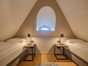 Ein kleiner, dreieckiger Raum mit zwei Betten, einem Oberlicht und einem Schreibtisch mit Lampe.