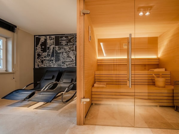 Un cuarto de sauna con bancos de madera y una puerta de vidrio, un mapa negro en la pared y una ventana que proporciona luz natural.
