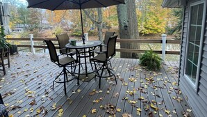 A covered patio with a table and chairs, surrounded by trees and a wooden deck. - By The Rivers Edge....remodeled cozy cottage (Geneva)