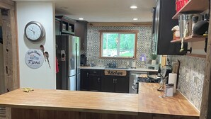 A modern kitchen with a wooden island, bar stools, a refrigerator, and a window with a view. - By The Rivers Edge....remodeled cozy cottage (Geneva)