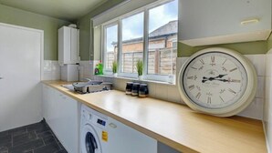 A modern kitchen with a built-in washing machine, a large window with a view of the outside, and a wall clock.