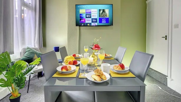 A dining area with a table set for breakfast, a TV mounted on the wall, and a potted plant.